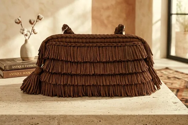 Borsa Favignana color cioccolato con quattro file di frange, su un piano in travertino