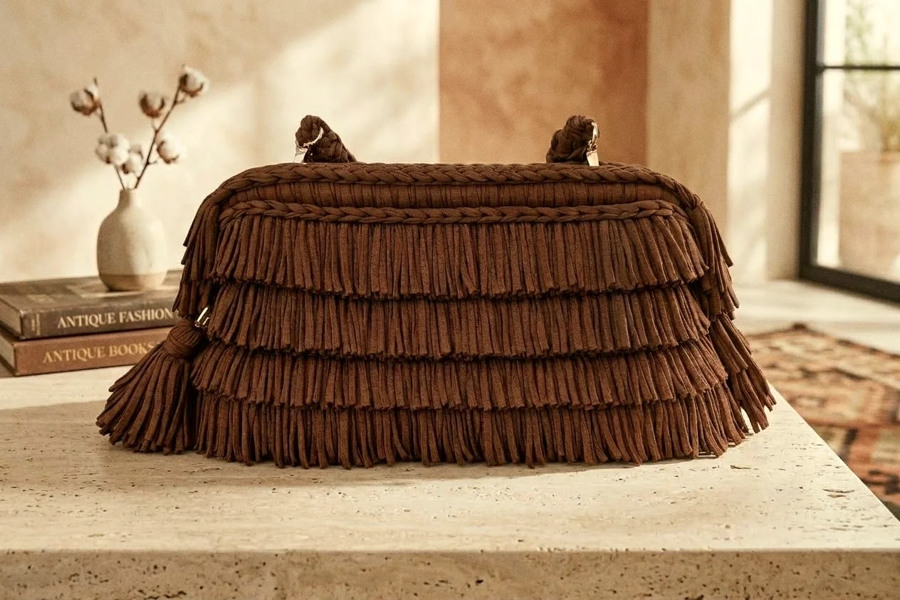 Borsa Favignana color cioccolato con quattro file di frange, su un piano in travertino