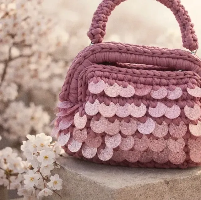 Borsa Ortigia rosa antico con paillettes, su un blocco di pietra tra fiori di ciliegio