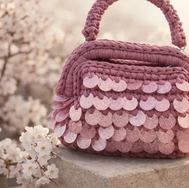 Borsa Ortigia rosa antico con paillettes, su un blocco di pietra tra fiori di ciliegio