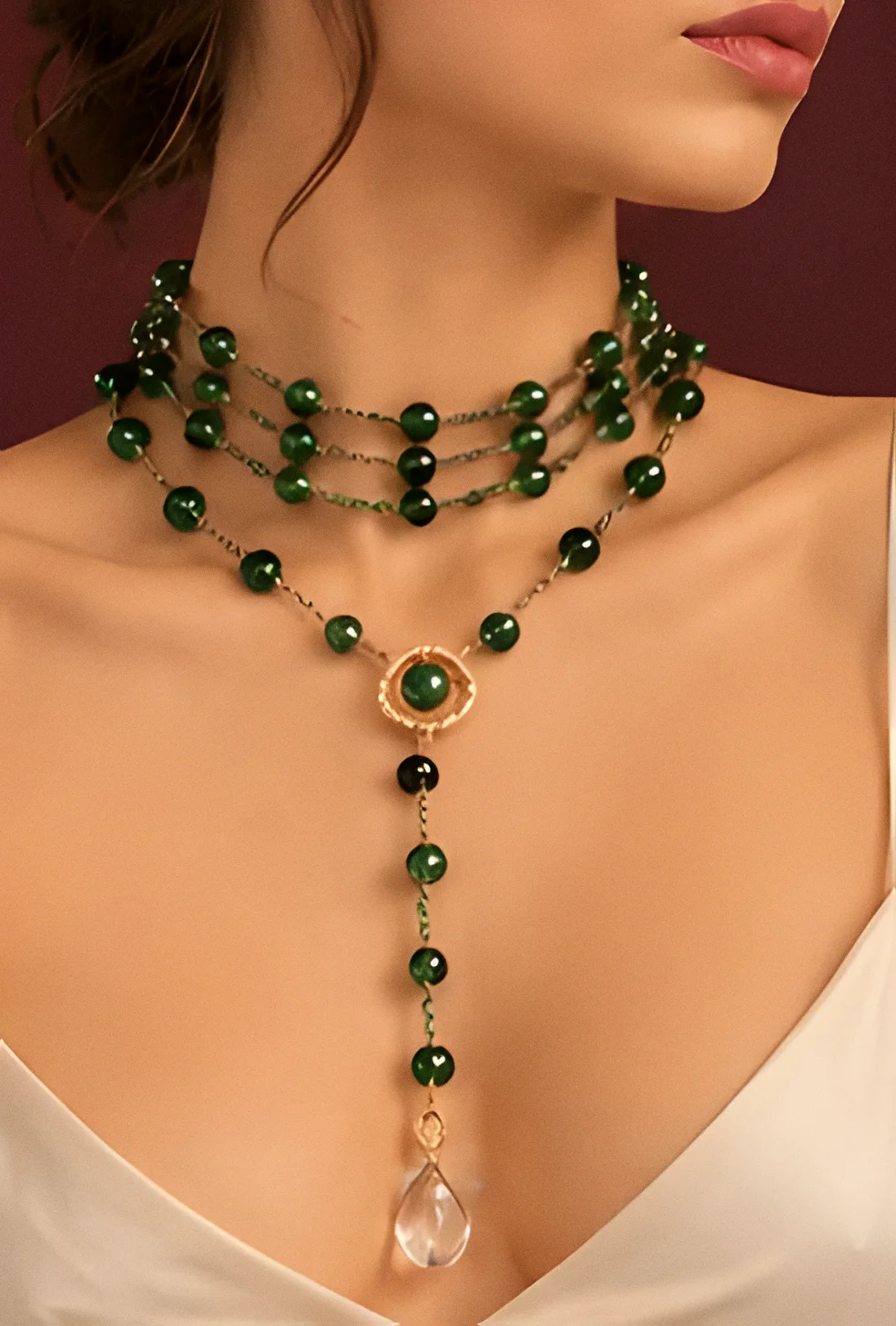Collana Stromboli smeraldo indossata come girocollo con medaglione dorato e goccia di cristallo, su un abito avorio